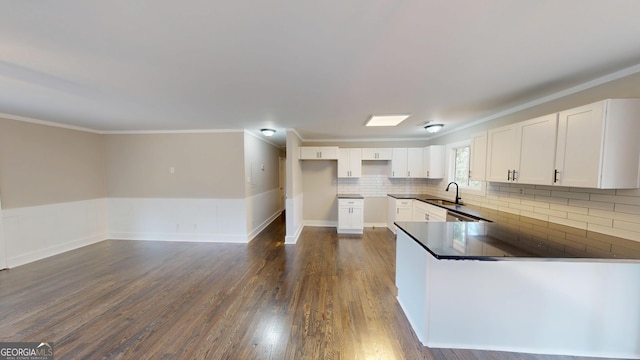 kitchen featuring a sink, dark countertops, dark wood finished floors, a peninsula, and white cabinets