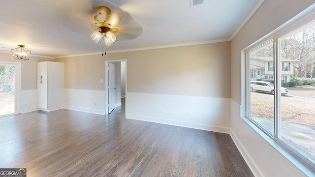 spare room featuring ceiling fan with notable chandelier, dark wood-type flooring, crown molding, and baseboards