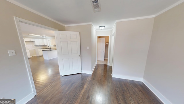 unfurnished room featuring dark wood-style floors, visible vents, baseboards, a sink, and crown molding