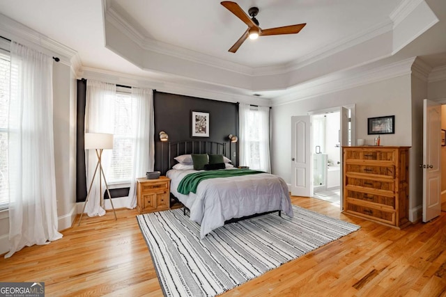 bedroom featuring a raised ceiling, light wood-type flooring, multiple windows, and ornamental molding