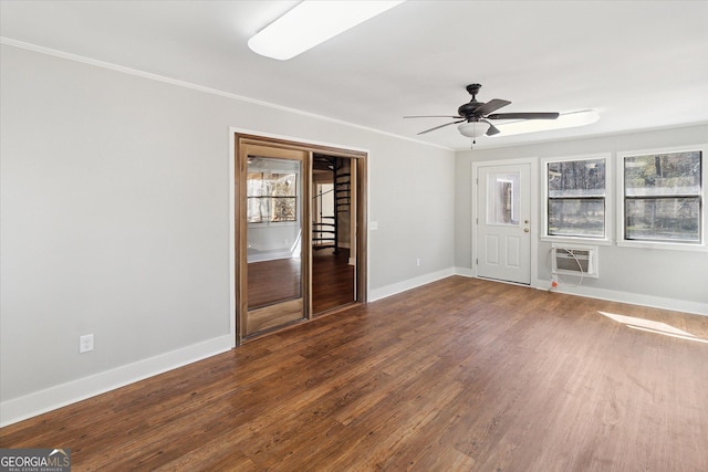 empty room featuring wood finished floors, ornamental molding, ceiling fan, a wall unit AC, and baseboards