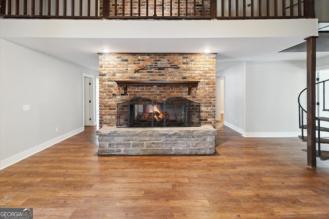 unfurnished living room with stairs, a brick fireplace, baseboards, and wood finished floors