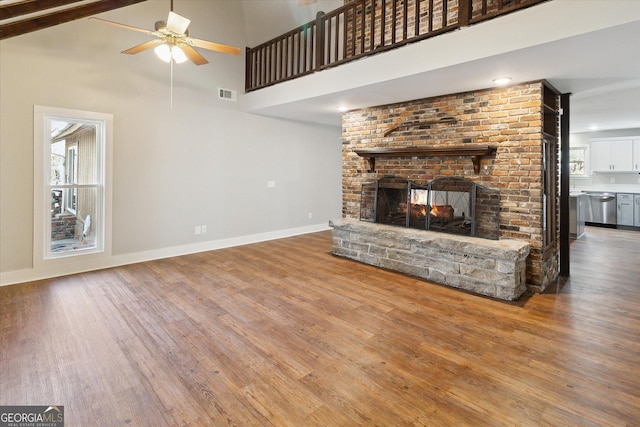 unfurnished living room featuring a brick fireplace, visible vents, wood finished floors, and ceiling fan