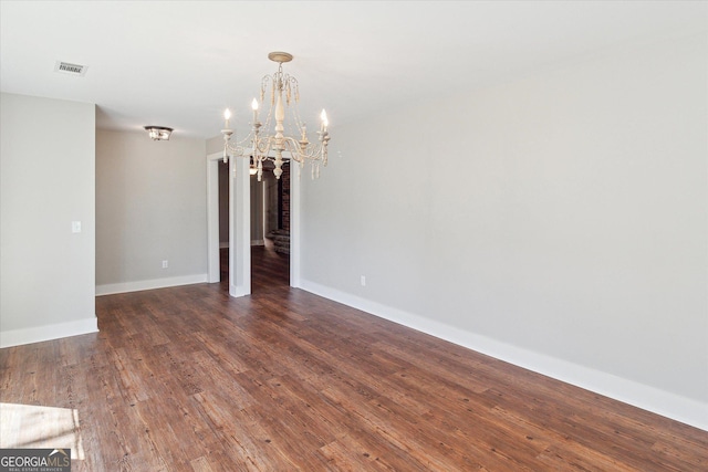 empty room with an inviting chandelier, baseboards, visible vents, and wood finished floors