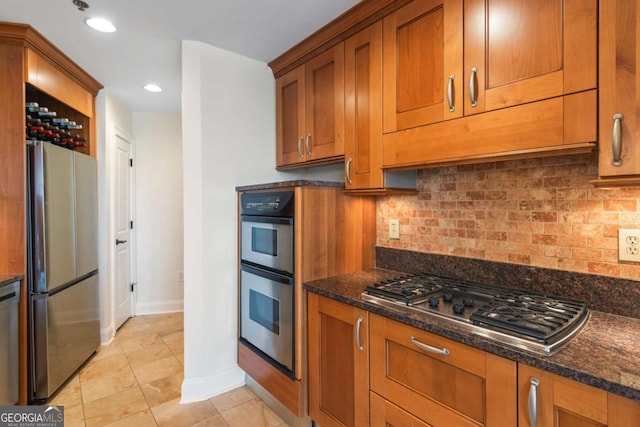 kitchen with baseboards, dark stone counters, decorative backsplash, brown cabinets, and stainless steel appliances