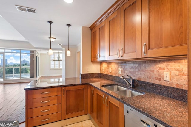 kitchen with visible vents, dark stone counters, dishwashing machine, brown cabinetry, and a sink