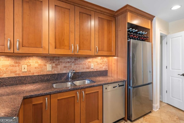 kitchen with dishwashing machine, brown cabinetry, dark stone counters, freestanding refrigerator, and a sink