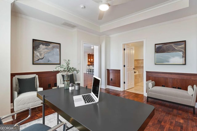 home office with a ceiling fan, visible vents, wood-type flooring, wainscoting, and a raised ceiling