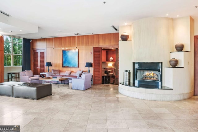 living room featuring visible vents, wood walls, and a warm lit fireplace