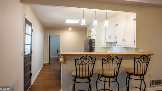 kitchen featuring visible vents, crown molding, dark wood-type flooring, a breakfast bar area, and white cabinetry