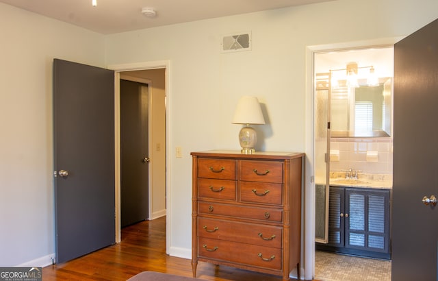 bedroom with visible vents, connected bathroom, baseboards, dark wood-style floors, and a sink