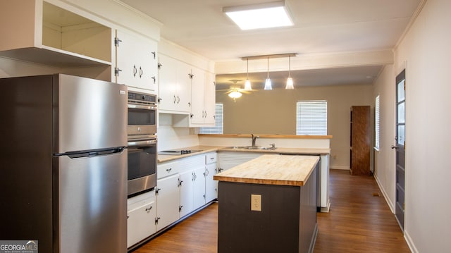 kitchen with butcher block countertops, a peninsula, stainless steel appliances, white cabinetry, and a sink