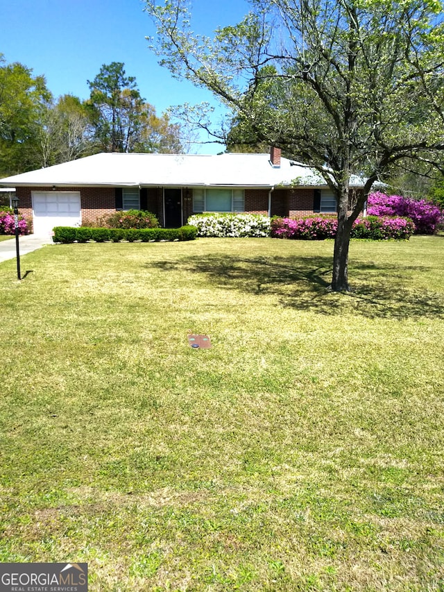 single story home with brick siding, a garage, a chimney, and a front yard