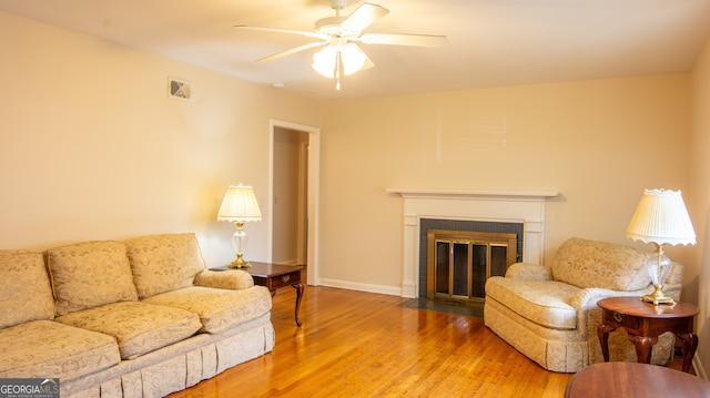 living room with visible vents, baseboards, ceiling fan, a fireplace, and wood finished floors