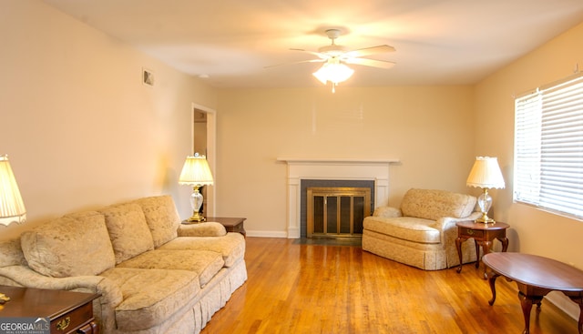 living room with a ceiling fan, wood finished floors, visible vents, baseboards, and a fireplace with flush hearth