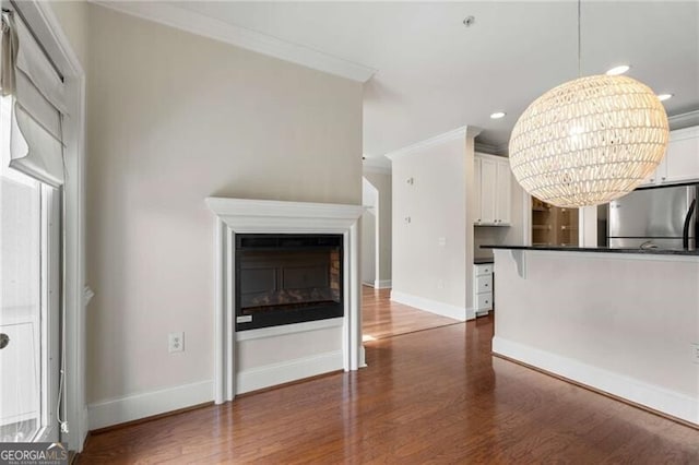 unfurnished living room with recessed lighting, dark wood finished floors, ornamental molding, baseboards, and a glass covered fireplace