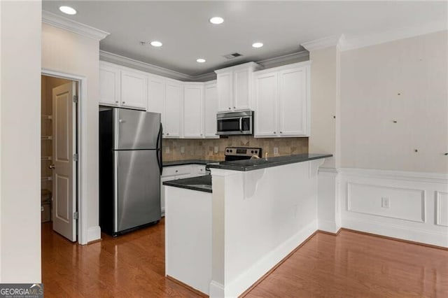 kitchen with dark countertops, a peninsula, appliances with stainless steel finishes, and crown molding