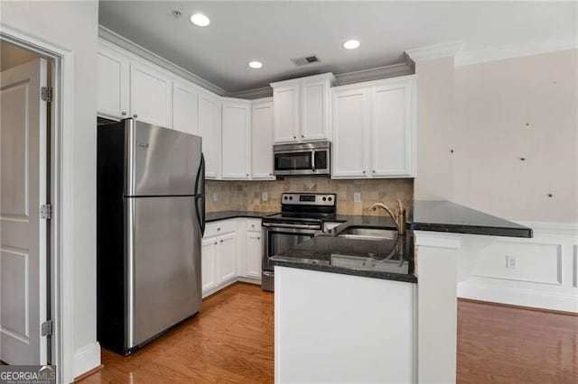 kitchen featuring stainless steel appliances, ornamental molding, a sink, light wood-style floors, and white cabinetry