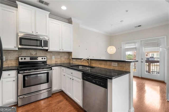 kitchen with a sink, a peninsula, appliances with stainless steel finishes, dark wood-type flooring, and visible vents