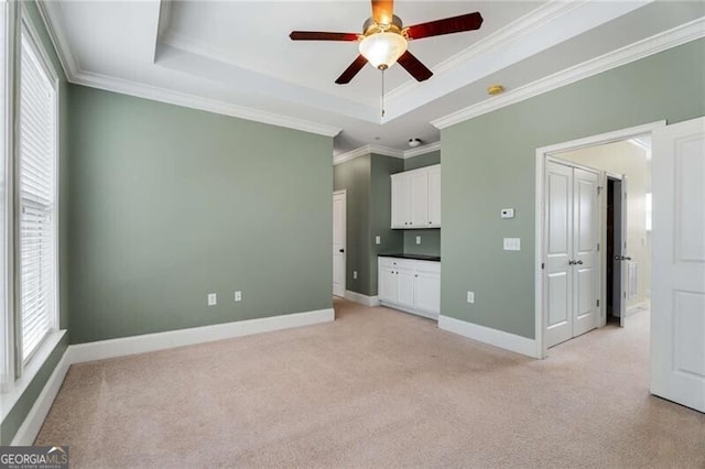 unfurnished bedroom with a raised ceiling, crown molding, baseboards, and light carpet