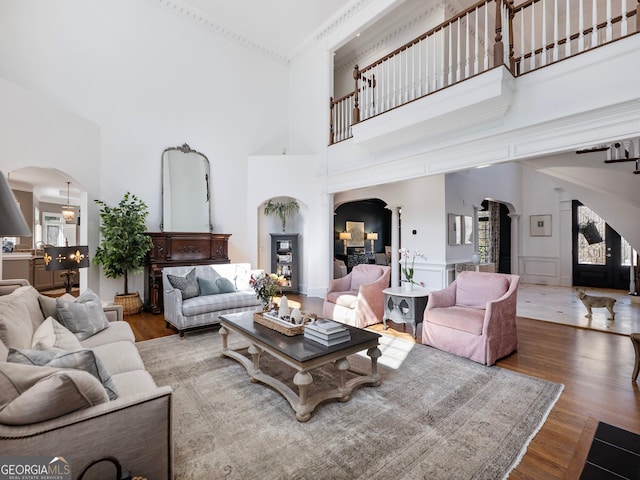 living area with a towering ceiling, arched walkways, and wood finished floors