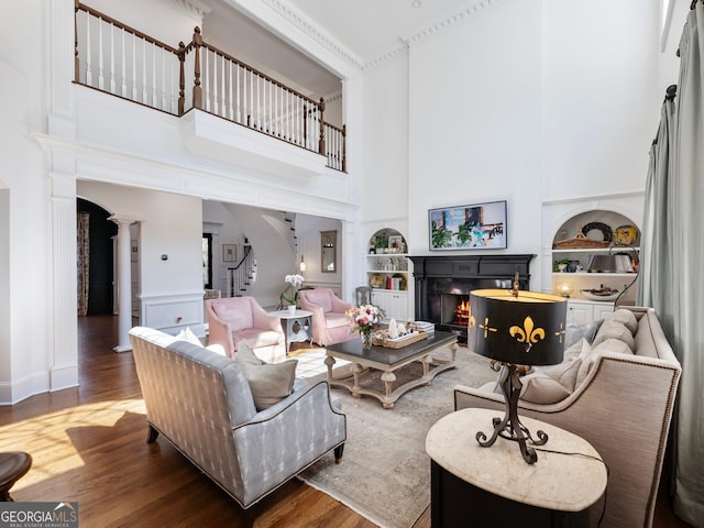 living area with stairs, a lit fireplace, built in shelves, wood finished floors, and ornate columns