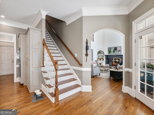 stairway featuring baseboards, wood finished floors, a warm lit fireplace, and crown molding