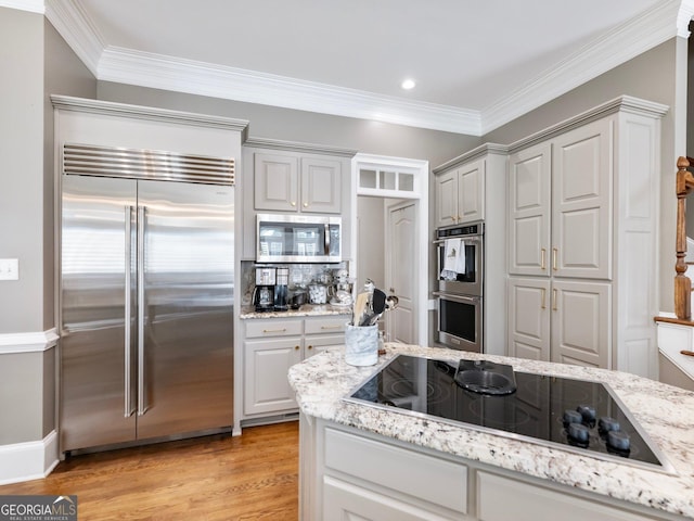 kitchen with light wood finished floors, light stone counters, ornamental molding, and appliances with stainless steel finishes