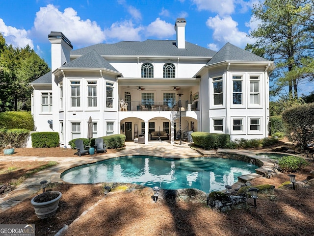 back of property with a ceiling fan, a balcony, a patio area, and a chimney