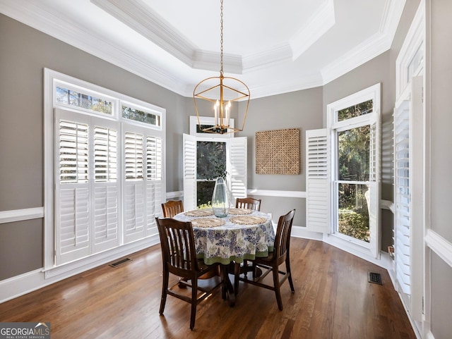 dining space featuring visible vents, a tray ceiling, wood finished floors, and a notable chandelier
