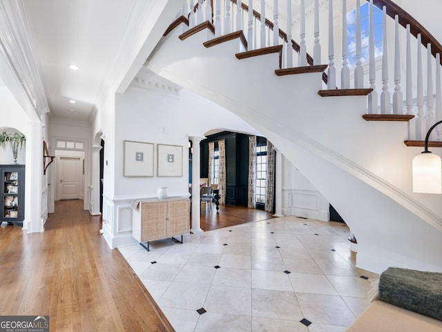 interior space featuring crown molding, tile patterned flooring, a decorative wall, arched walkways, and ornate columns