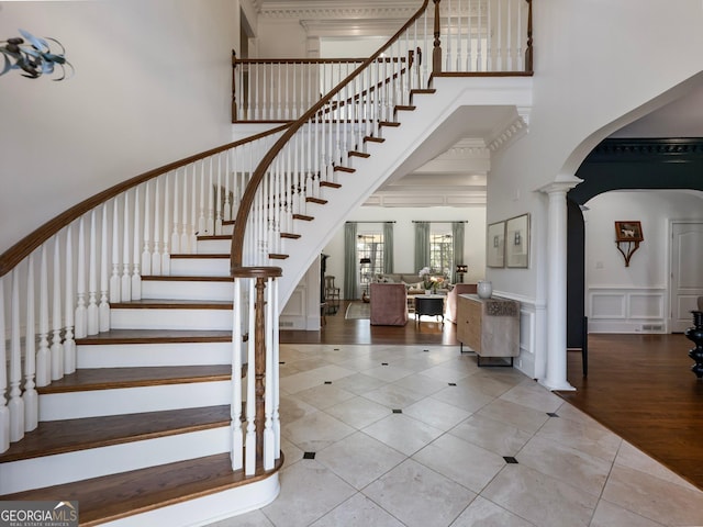 foyer entrance featuring stairs, decorative columns, a decorative wall, arched walkways, and a towering ceiling