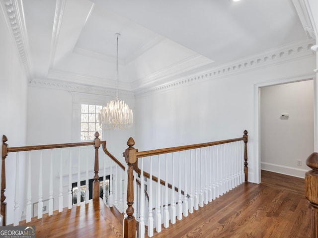 hallway with an upstairs landing, a tray ceiling, a notable chandelier, and wood finished floors