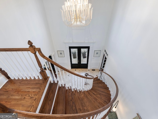 stairs with an inviting chandelier, french doors, a high ceiling, and wood finished floors