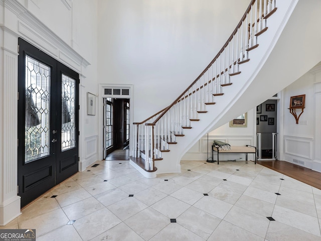 entryway featuring a decorative wall, visible vents, stairway, a high ceiling, and french doors
