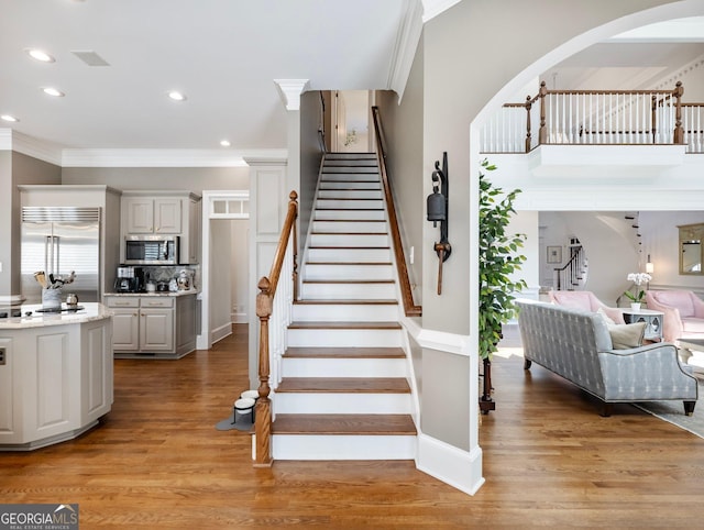 staircase with arched walkways, wood finished floors, recessed lighting, and crown molding
