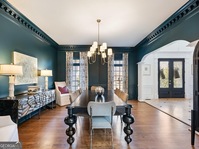 dining area featuring a notable chandelier, crown molding, arched walkways, and wood finished floors