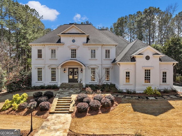 view of front facade with stucco siding, french doors, and roof with shingles