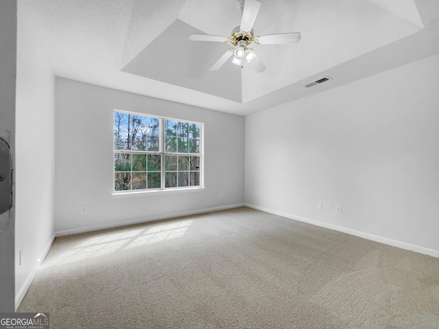 carpeted spare room with visible vents, baseboards, a raised ceiling, and a ceiling fan