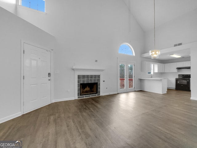 unfurnished living room featuring wood finished floors, visible vents, high vaulted ceiling, a tile fireplace, and french doors