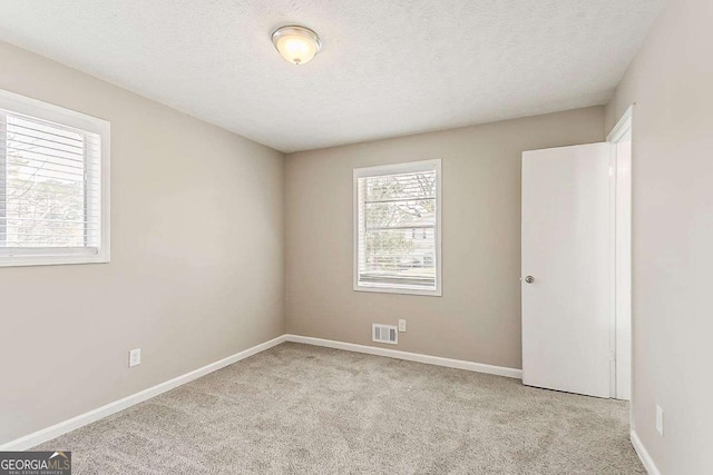 carpeted empty room with visible vents, a textured ceiling, and baseboards