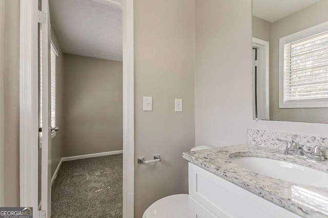 half bath featuring toilet, vanity, and baseboards