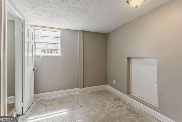 spare room featuring baseboards, unfinished concrete flooring, and a textured ceiling