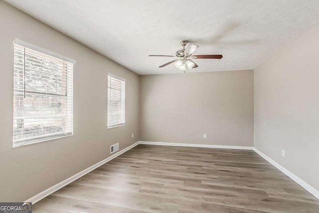unfurnished room with wood finished floors, baseboards, visible vents, ceiling fan, and a textured ceiling