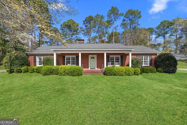 ranch-style house featuring a chimney, brick siding, a porch, and a front lawn