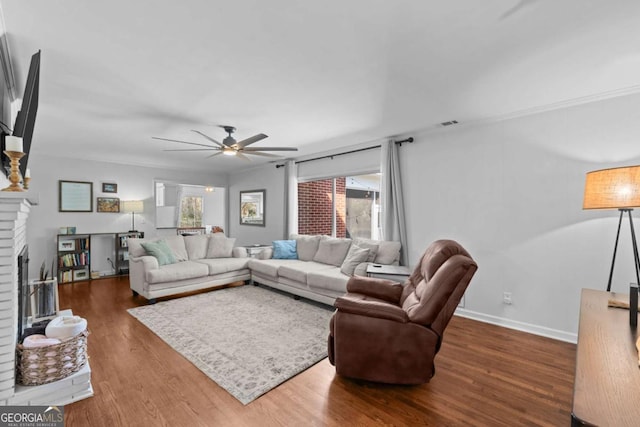 living room with wood finished floors, visible vents, baseboards, ceiling fan, and a brick fireplace