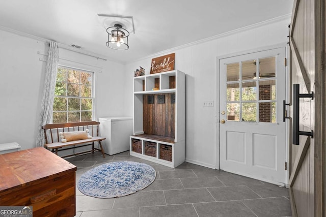 mudroom with dark tile patterned floors and crown molding