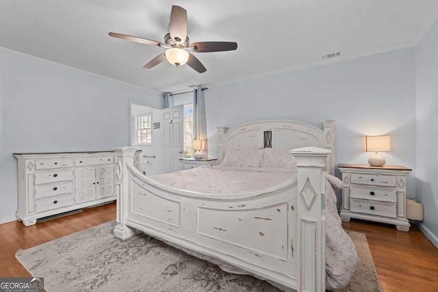 bedroom with baseboards, wood finished floors, visible vents, and ornamental molding