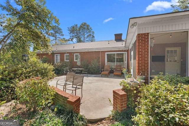 back of property featuring brick siding, a patio area, and a chimney