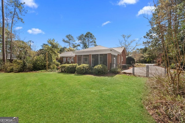 back of property featuring a gate, fence, a sunroom, a lawn, and brick siding